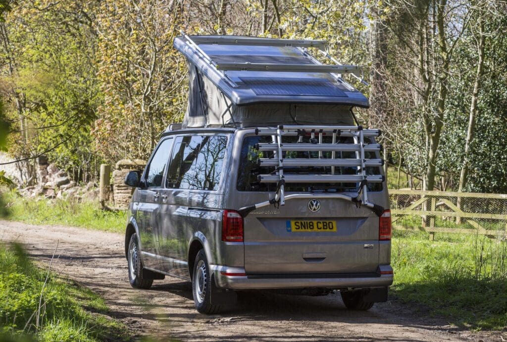 Campervan with a Pop Top Roof on the road with trees and grass in the background