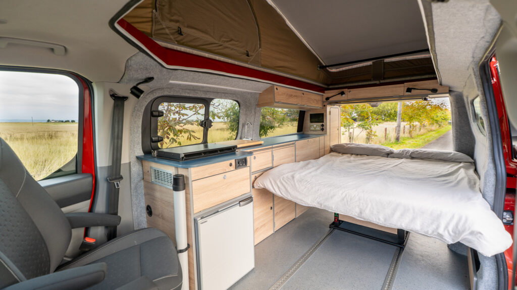 Bed setup with tailgate open, blue worktop kitchen and overhead lockers.