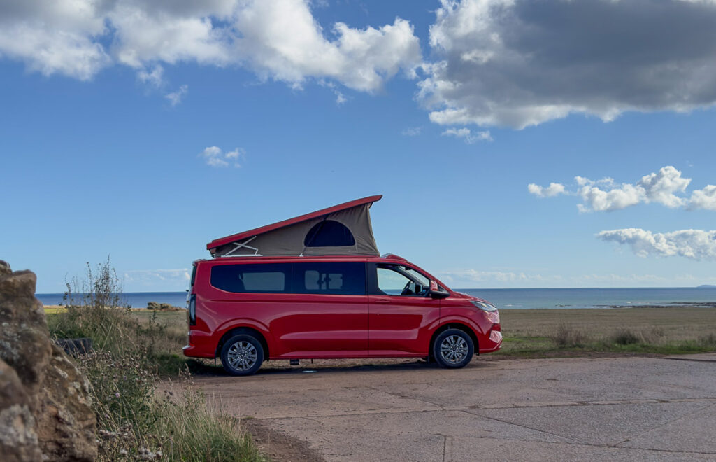 A red Ford Transit Custom Camper van parked in front of a blue sky.