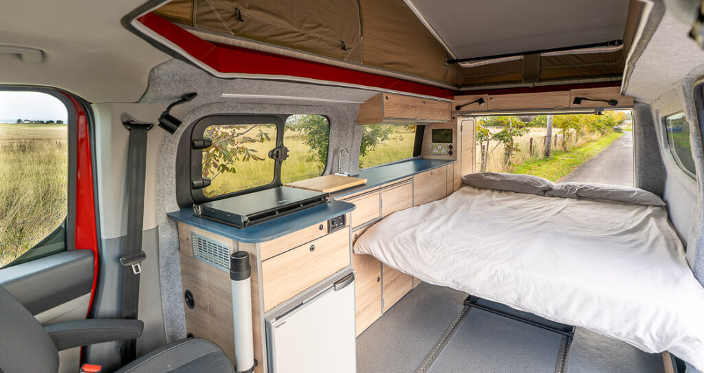 Wide interior view showing pop-top roof, kitchen pod and made-up bed.