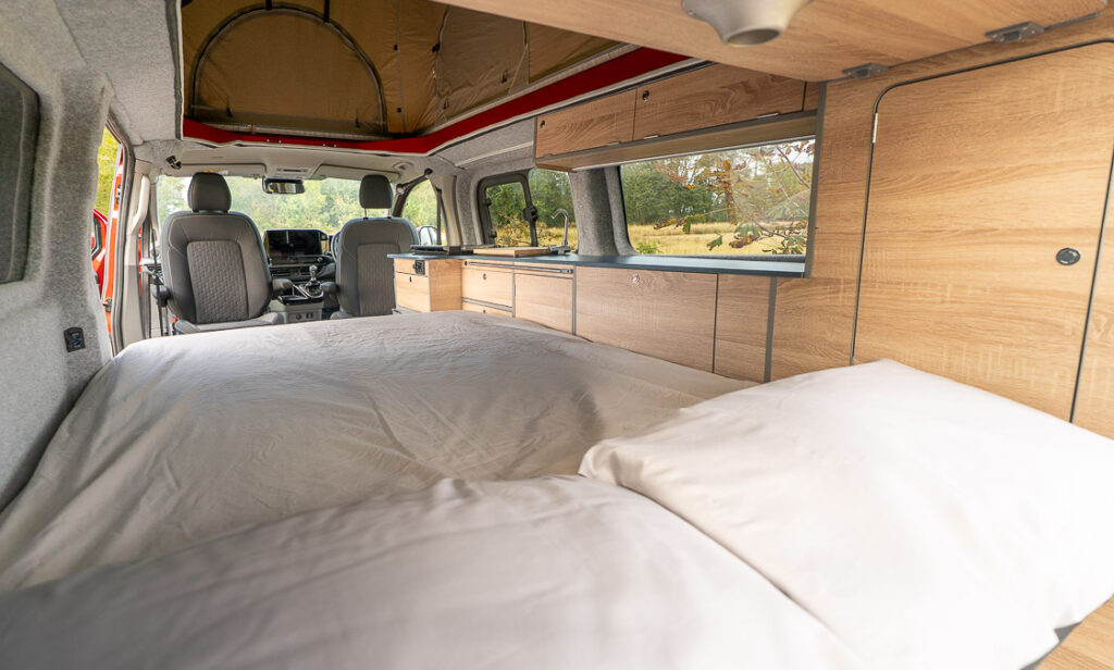 View from rear bed toward cab, showing cabinets, sink and open roof.