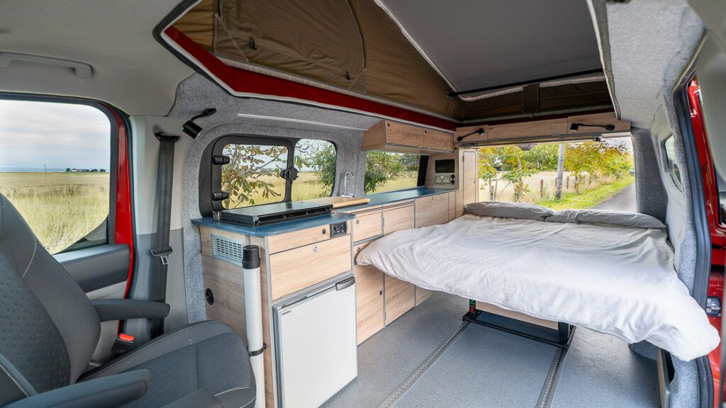 Bed setup with tailgate open, blue worktop kitchen and overhead lockers.