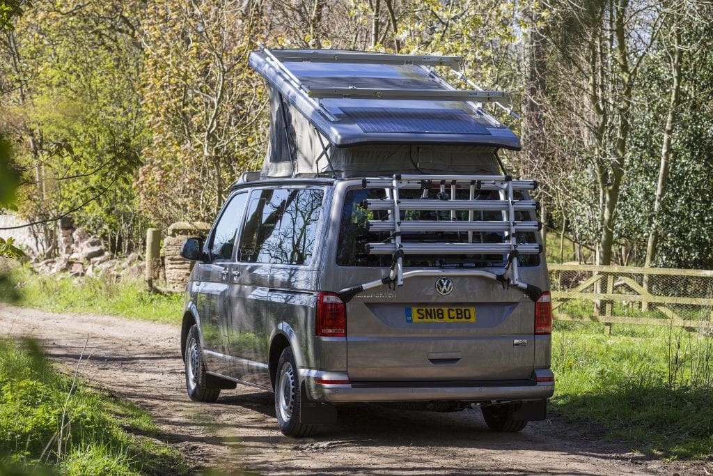 Campervan with a Pop Top Roof on the road with trees and grass on the background